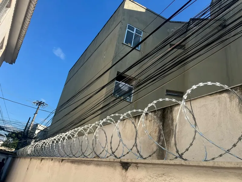 Concertina em espiral no alto de um muro, com fios de poste e um prédio atrás