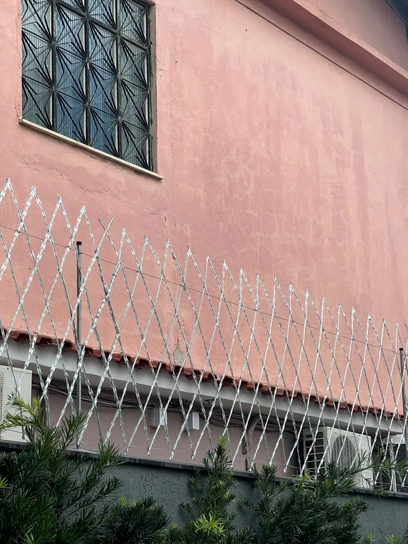 Rede laminada em losangos instalada no alto do muro de uma casa de parede rosa